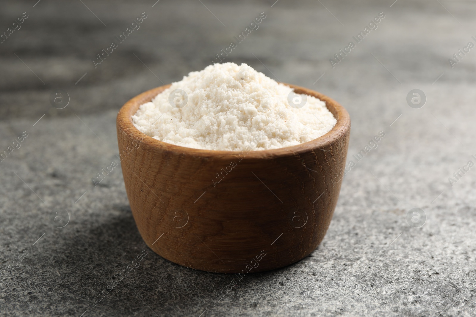 Photo of Organic coconut flour in bowl on grey table, closeup