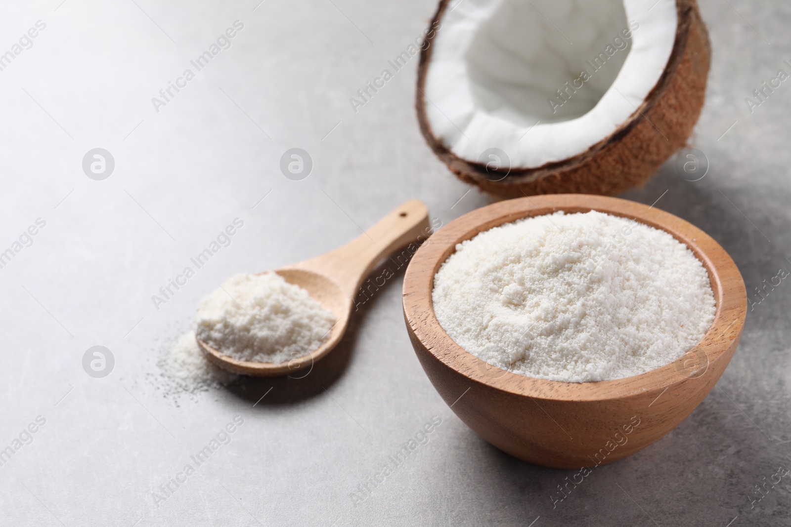 Photo of Coconut flour in bowl, spoon and fresh fruit on light grey table