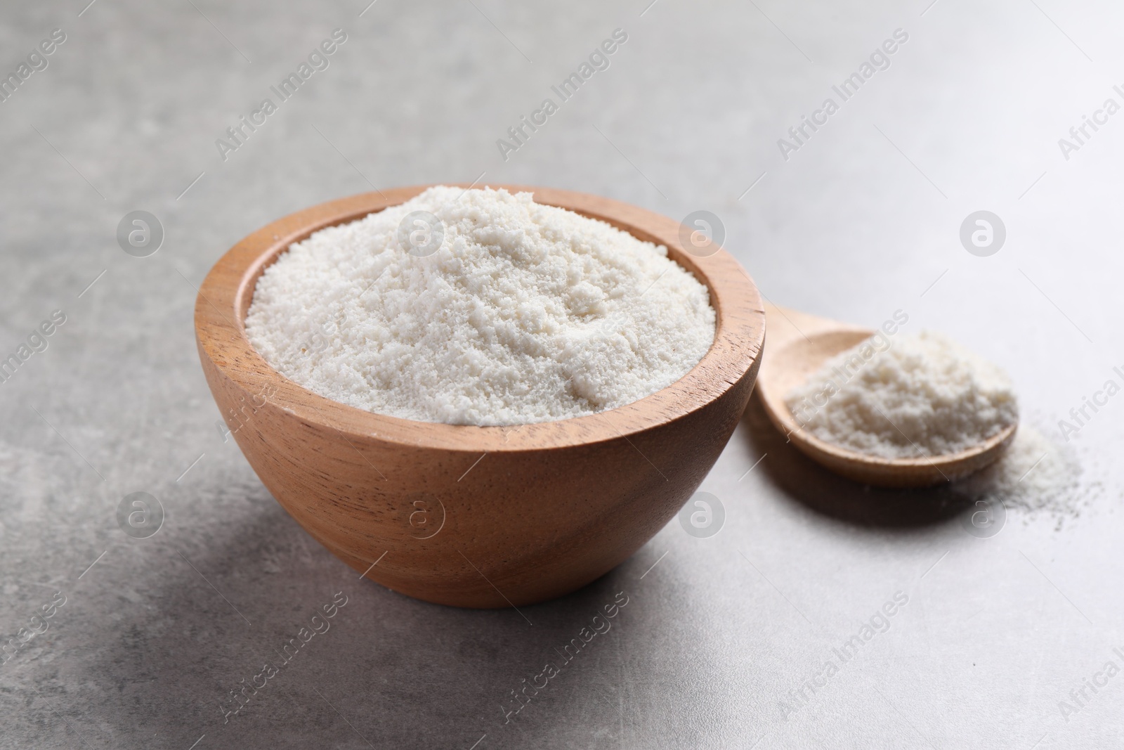 Photo of Coconut flour in bowl and spoon on light grey table, closeup