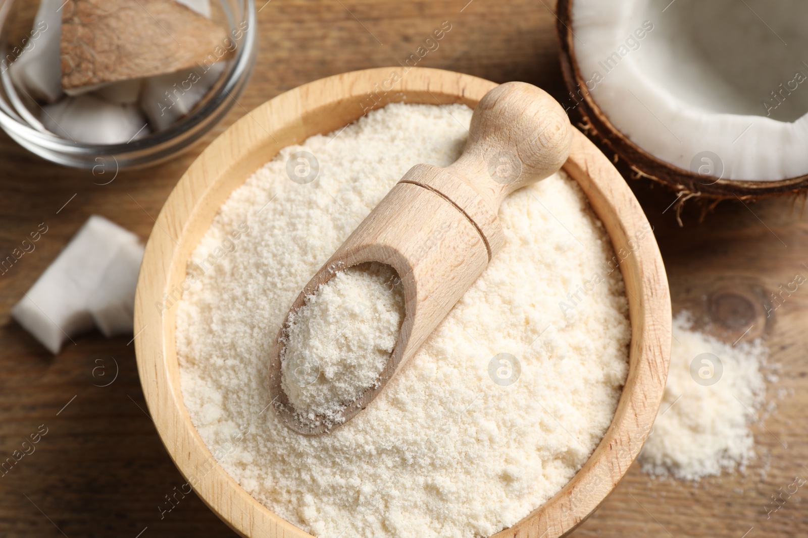 Photo of Coconut flour in bowl, scoop and fresh fruits on wooden table, flat lay