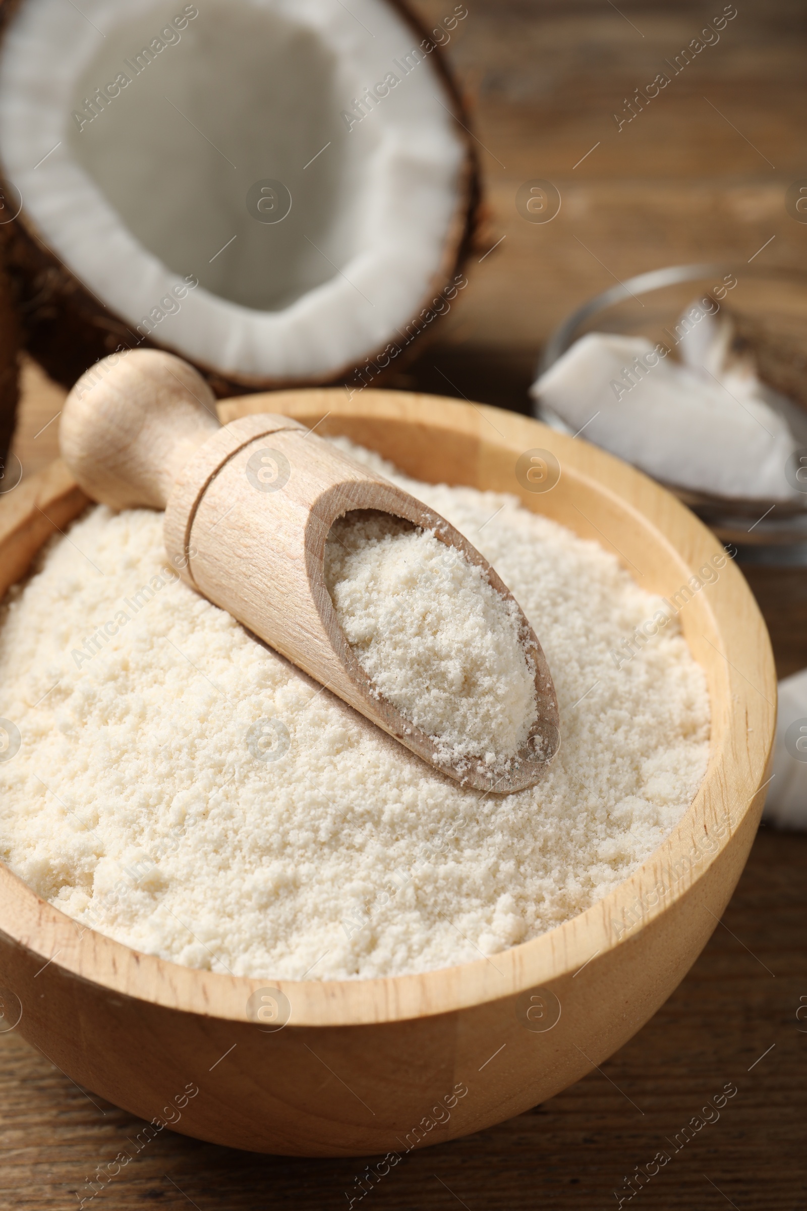 Photo of Coconut flour in bowl and scoop on wooden table, closeup