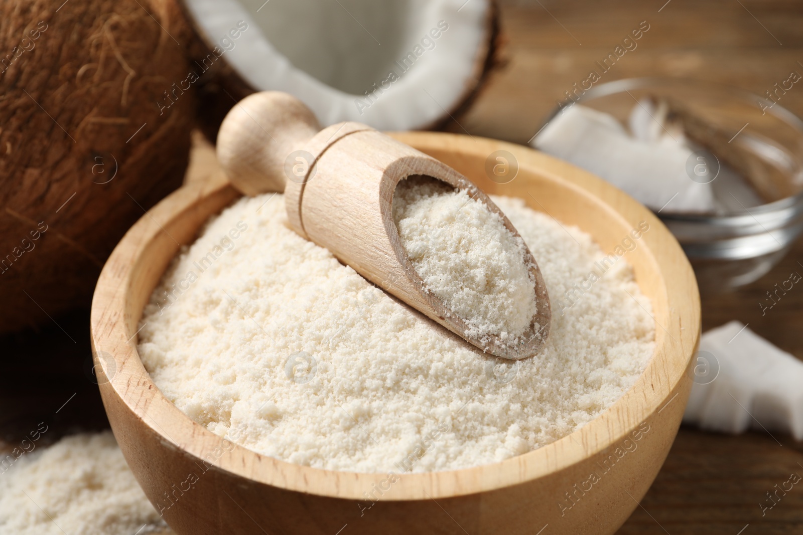 Photo of Coconut flour in bowl and scoop on wooden table, closeup