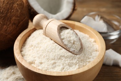 Photo of Coconut flour in bowl and scoop on wooden table, closeup