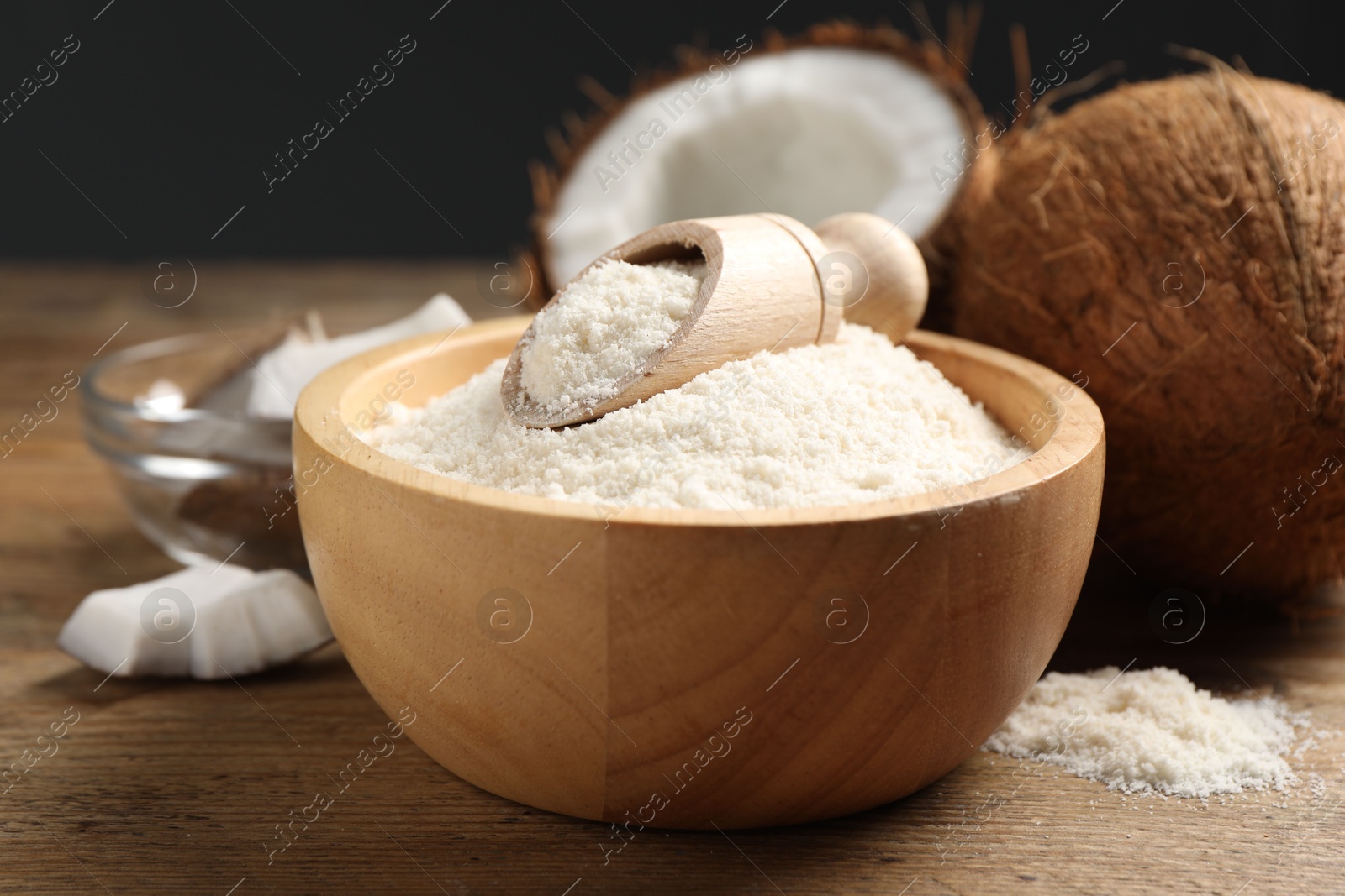 Photo of Coconut flour in bowl, scoop and fresh fruits on wooden table, closeup