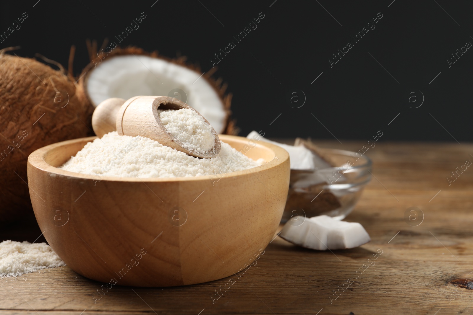 Photo of Coconut flour in bowl, scoop and fresh fruits on wooden table, closeup. Space for text