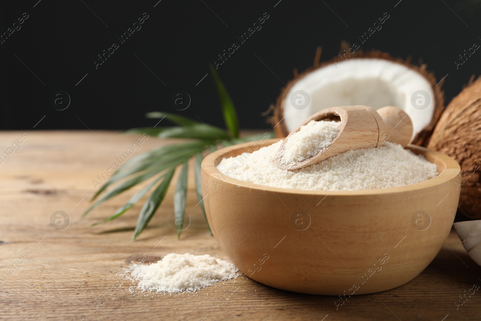 Photo of Coconut flour in bowl, scoop and fresh fruits on wooden table, closeup. Space for text