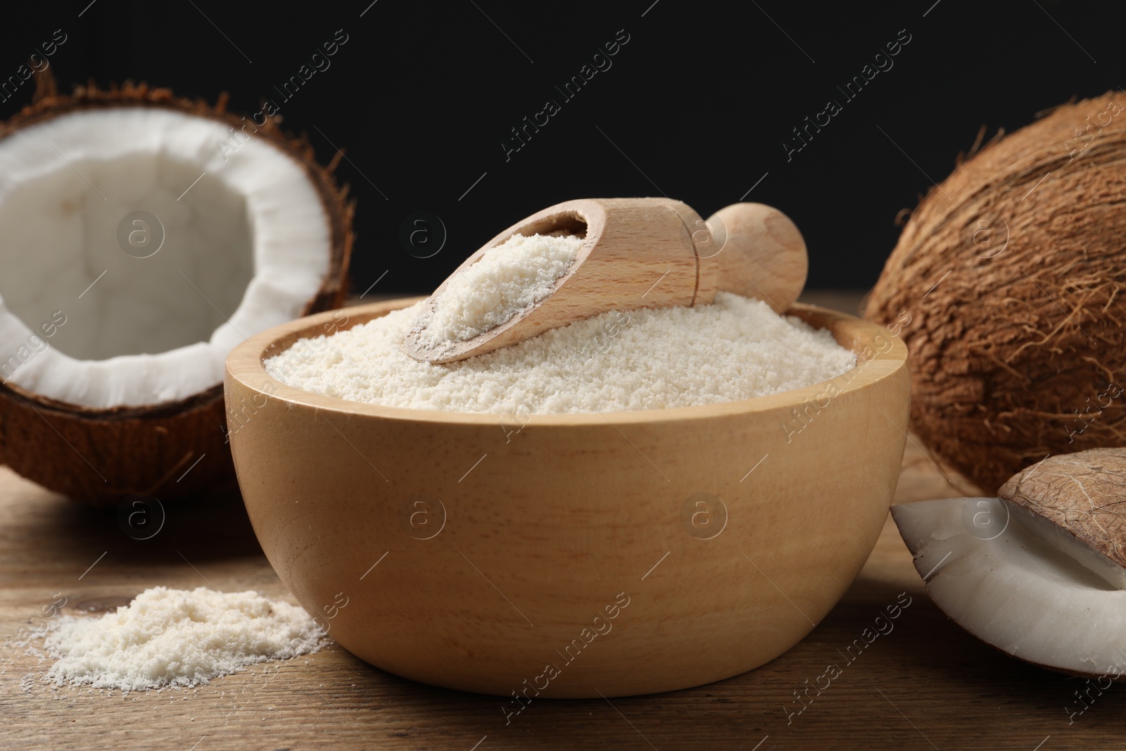 Photo of Coconut flour in bowl, scoop and fresh fruits on wooden table, closeup