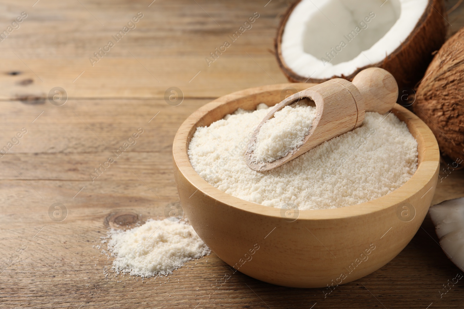 Photo of Coconut flour in bowl, scoop and fresh fruits on wooden table, closeup. Space for text