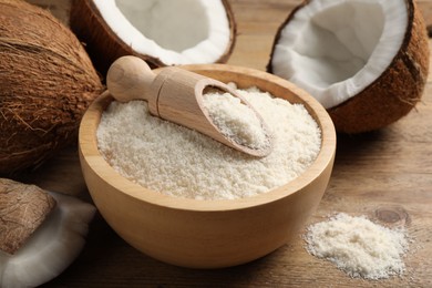 Photo of Coconut flour in bowl, scoop and fresh fruits on wooden table, closeup