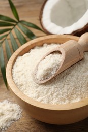 Photo of Coconut flour in bowl and scoop on wooden table, closeup