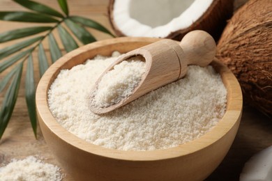 Photo of Coconut flour in bowl, scoop and fresh fruits on wooden table, closeup