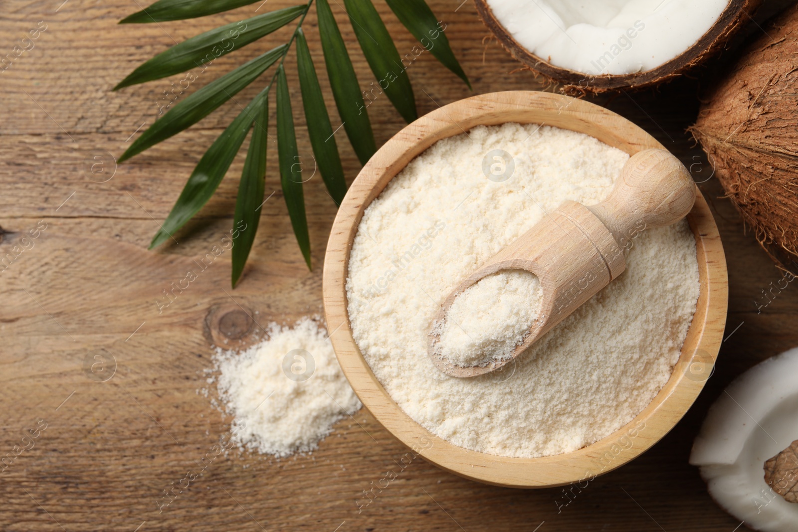 Photo of Coconut flour in bowl, scoop, fresh fruits and leaf on wooden table, flat lay