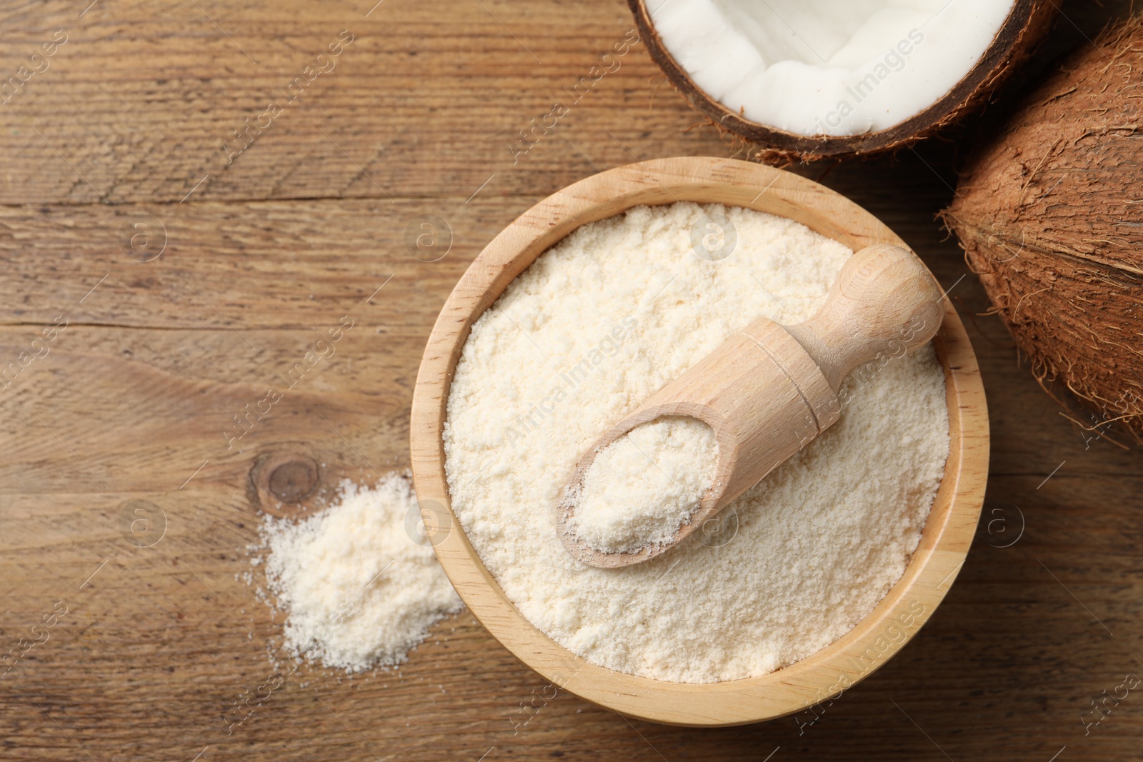 Photo of Coconut flour in bowl, scoop and fresh fruits on wooden table, flat lay. Space for text