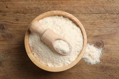 Photo of Organic coconut flour in bowl and scoop on wooden table, top view