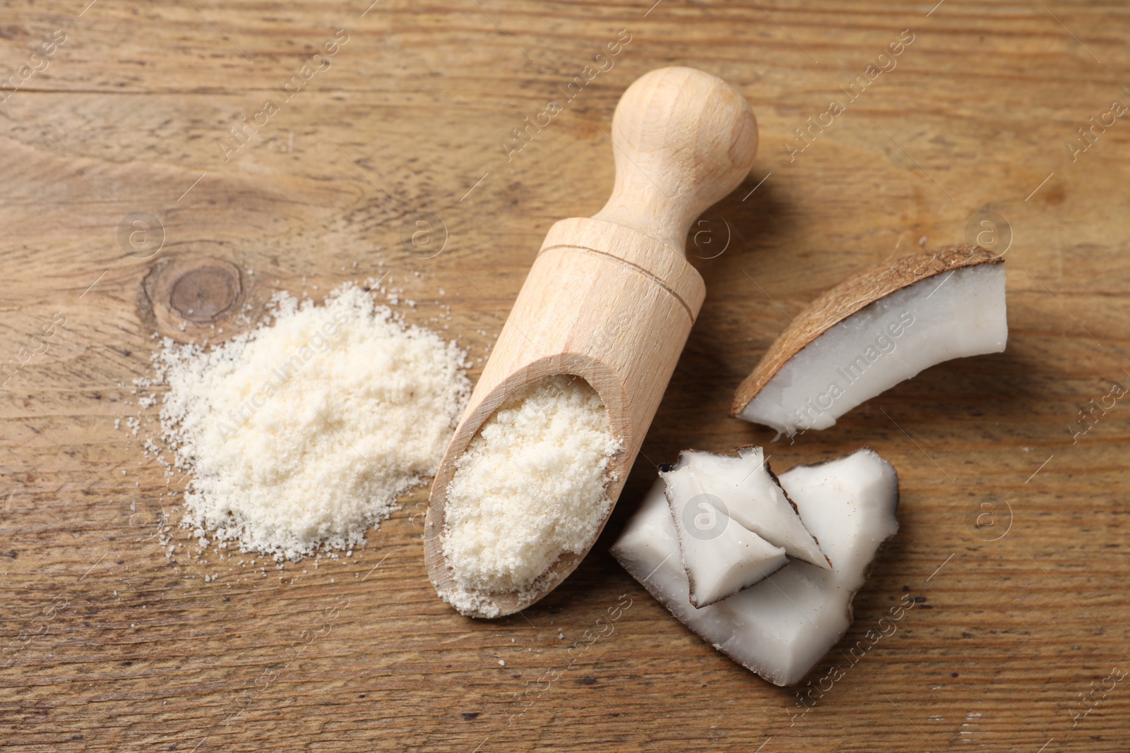 Photo of Organic coconut flour in scoop and fruit pieces on wooden table, flat lay