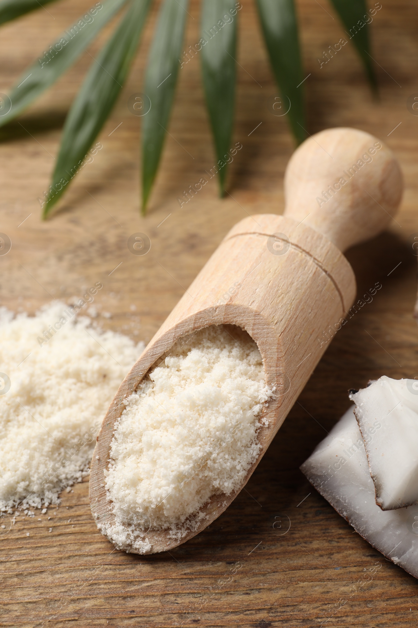 Photo of Coconut flour in scoop and leaf on wooden table, closeup