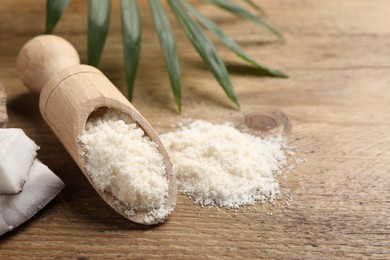 Photo of Coconut flour in scoop and leaf on wooden table, closeup. Space for text