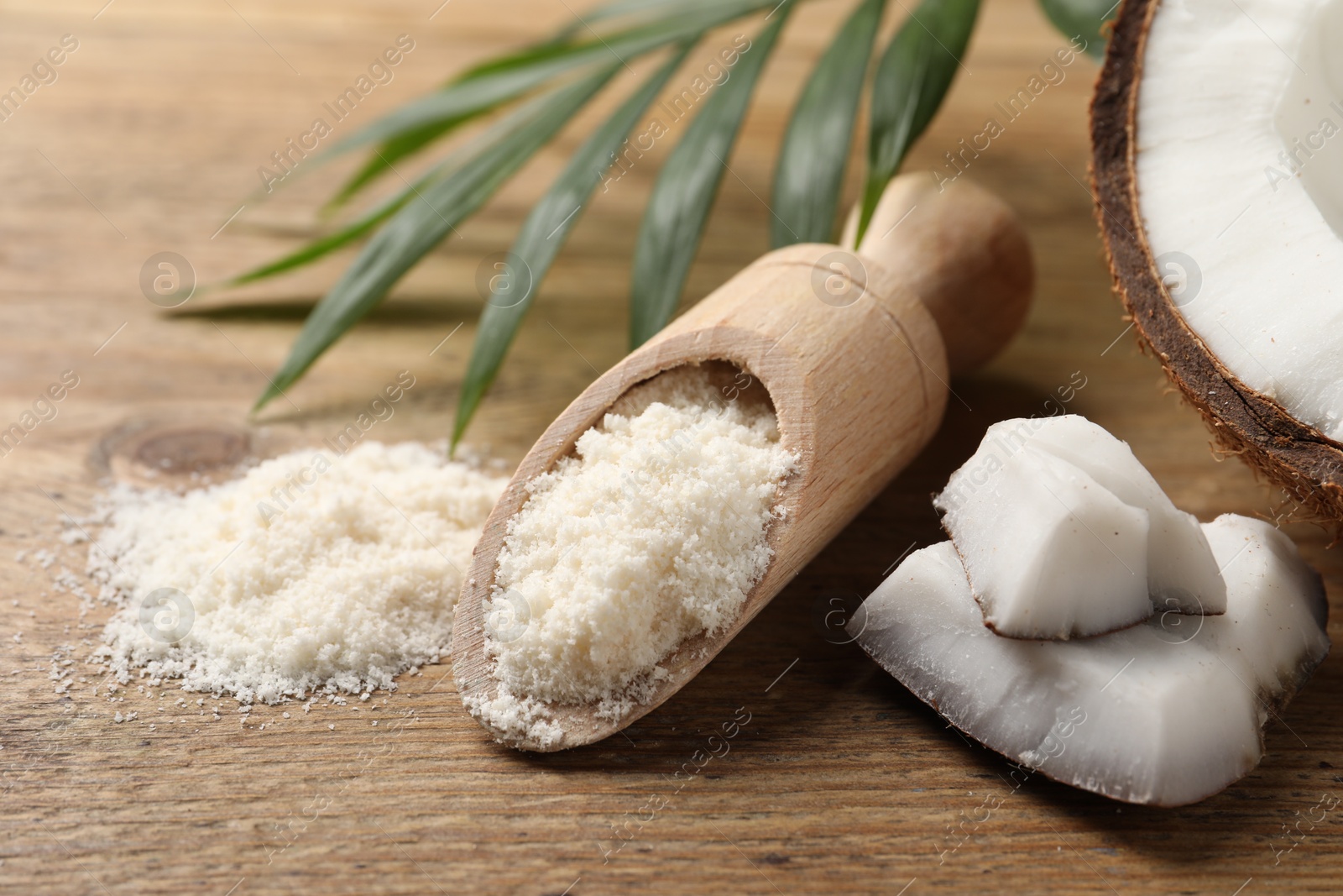 Photo of Coconut flour in scoop, fresh fruits and leaf on wooden table, closeup