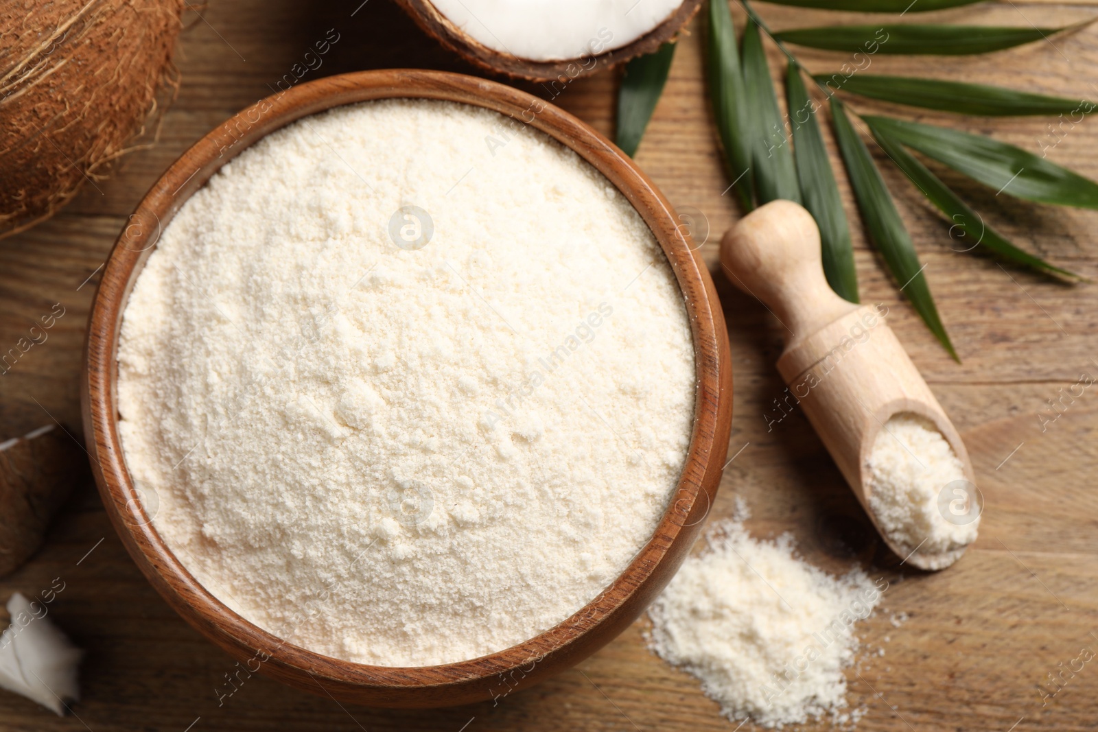 Photo of Coconut flour in bowl and scoop on wooden table, flat lay