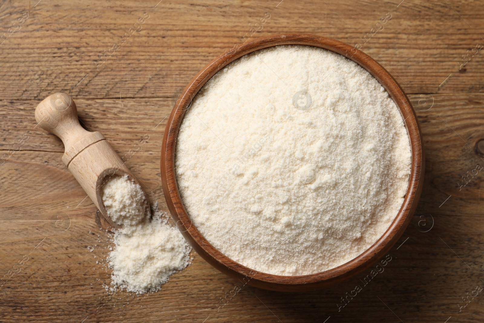 Photo of Coconut flour in bowl and scoop on wooden table, flat lay