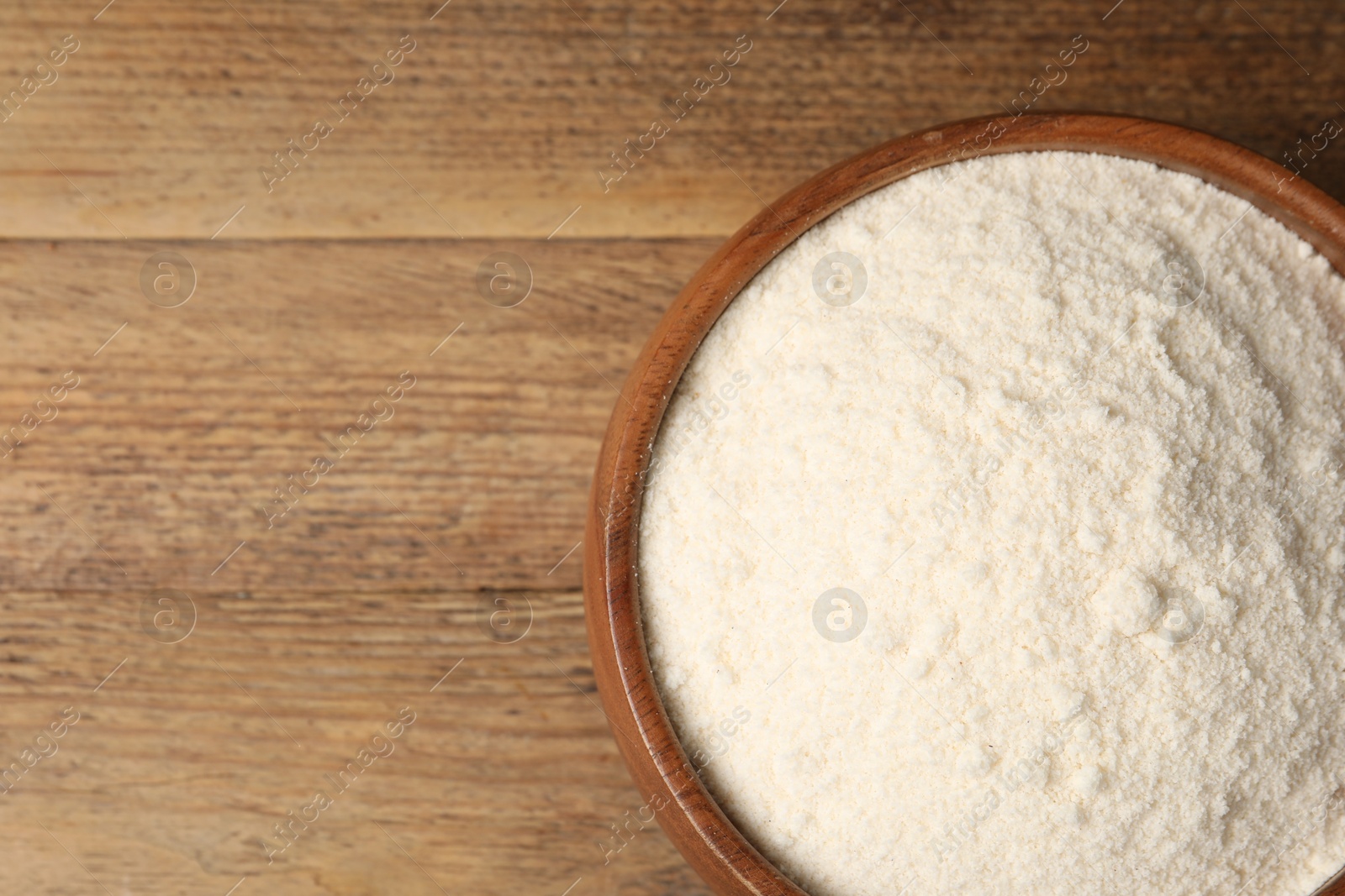 Photo of Coconut flour in bowl on wooden table, top view. Space for text