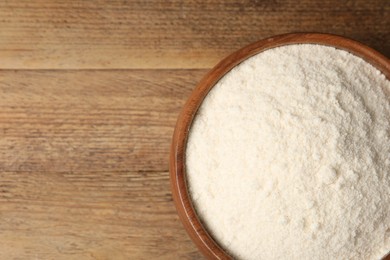 Photo of Coconut flour in bowl on wooden table, top view. Space for text