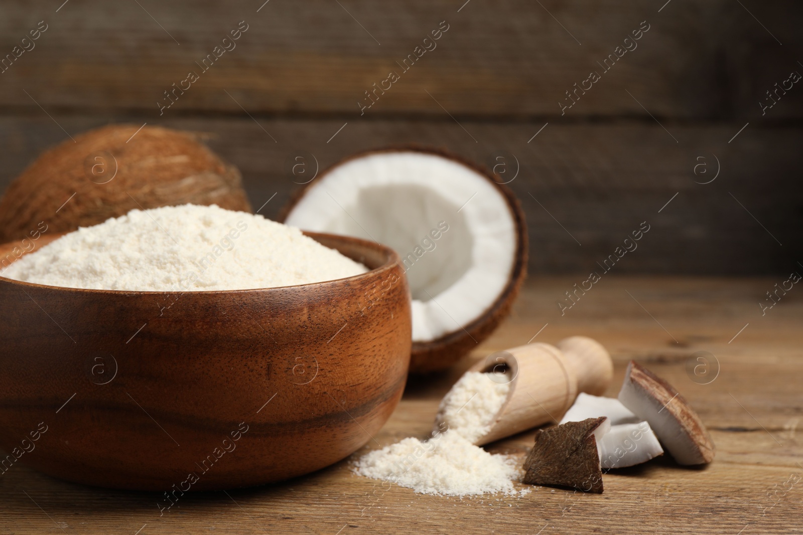 Photo of Coconut flour in bowl, scoop and fresh fruits on wooden table, closeup. Space for text