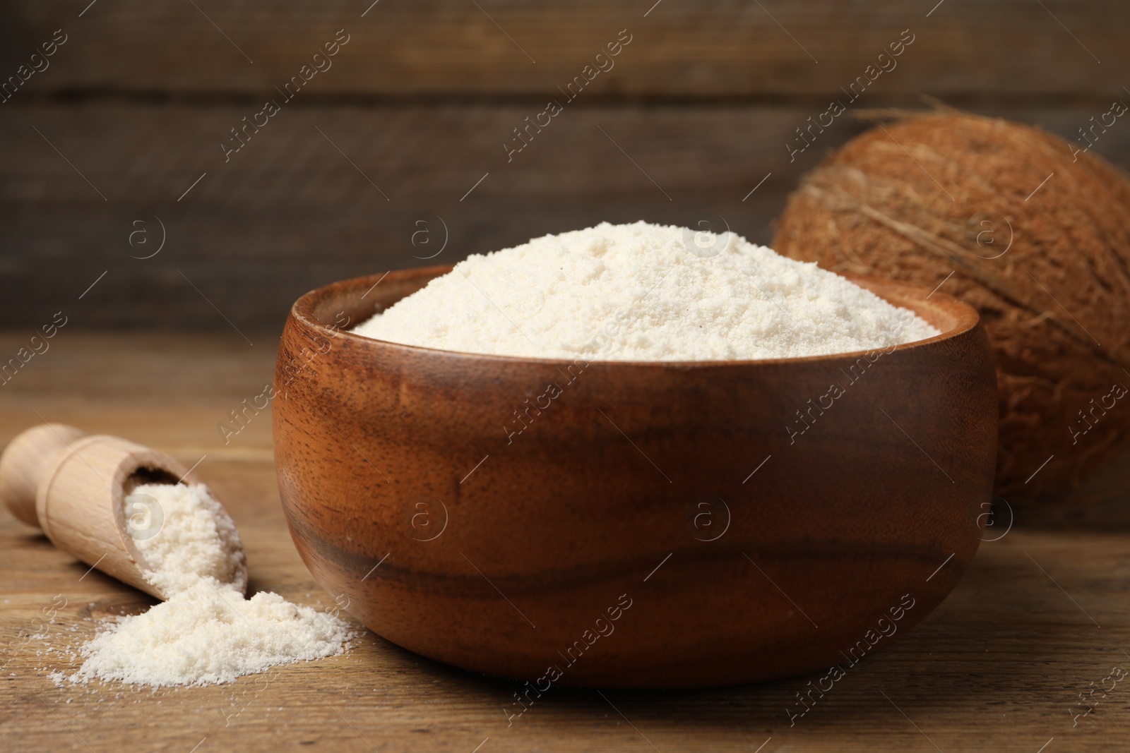 Photo of Coconut flour in bowl, scoop and fresh fruits on wooden table, closeup