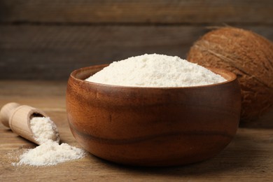 Photo of Coconut flour in bowl, scoop and fresh fruits on wooden table, closeup