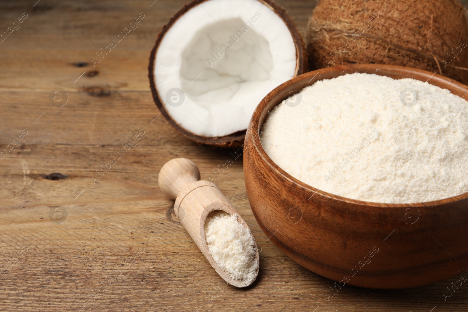 Photo of Coconut flour in bowl, scoop and fresh fruits on wooden table, closeup. Space for text