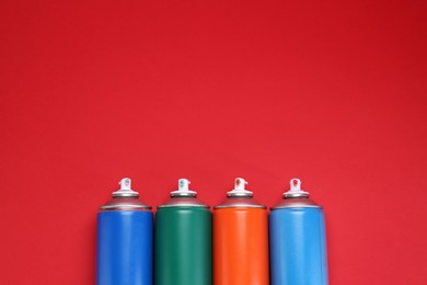 Many spray paint cans on red background, top view. Space for text