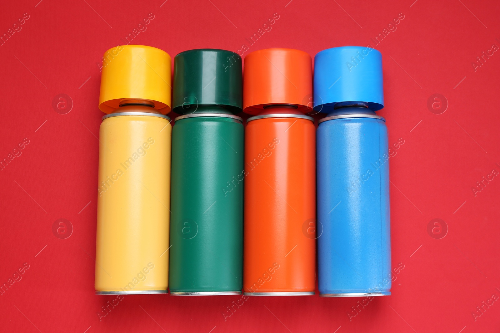 Photo of Many spray paint cans on red background, top view