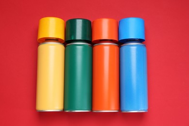 Photo of Many spray paint cans on red background, top view