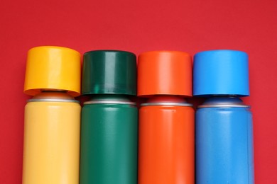 Many spray paint cans on red background, top view