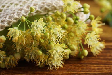 Photo of Fresh linden leaves and flowers on wooden table, closeup