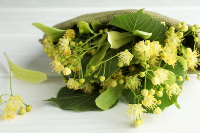 Fresh linden leaves and flowers on white wooden table, closeup