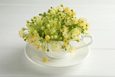 Photo of Fresh linden leaves and flowers in cup on white wooden table