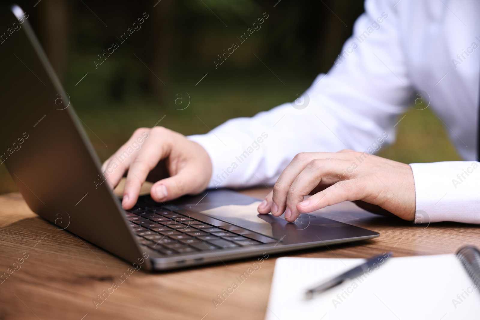 Photo of Businessman working with laptop at table outdoors, closeup. Remote job