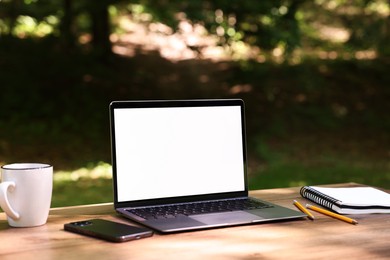 Photo of Laptop, notebook, pencils, cup and smartphone on wooden table outdoors. Remote work