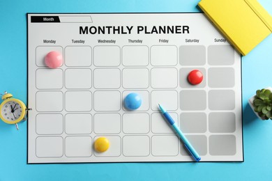 Photo of Timetable. Monthly planner, pen, drawing pins and alarm clock on light blue background, top view