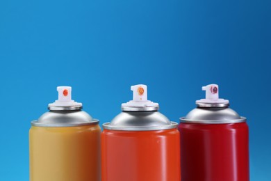 Three spray paint cans on light blue background, closeup. Space for text