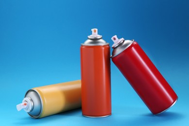 Photo of Three spray paint cans on light blue background