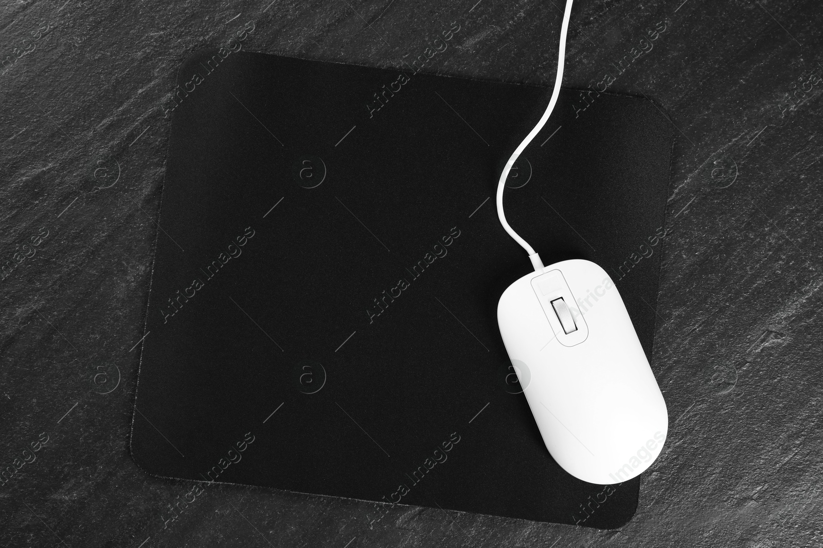 Photo of White wired mouse and mousepad on black textured table, top view