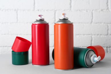 Cans of spray paint on wooden table near white brick wall