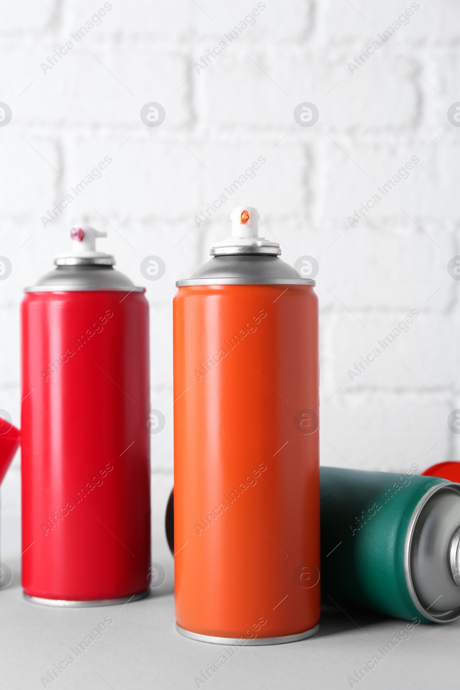 Photo of Cans of spray paint on wooden table near white brick wall