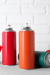 Cans of spray paint on wooden table near white brick wall