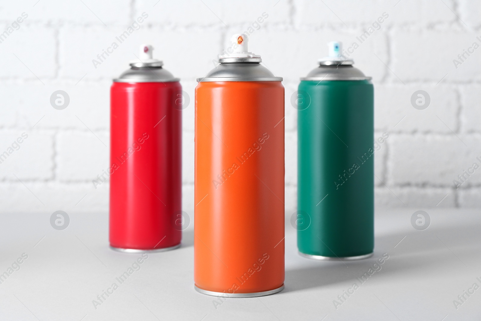 Photo of Cans of spray paint on wooden table near white brick wall