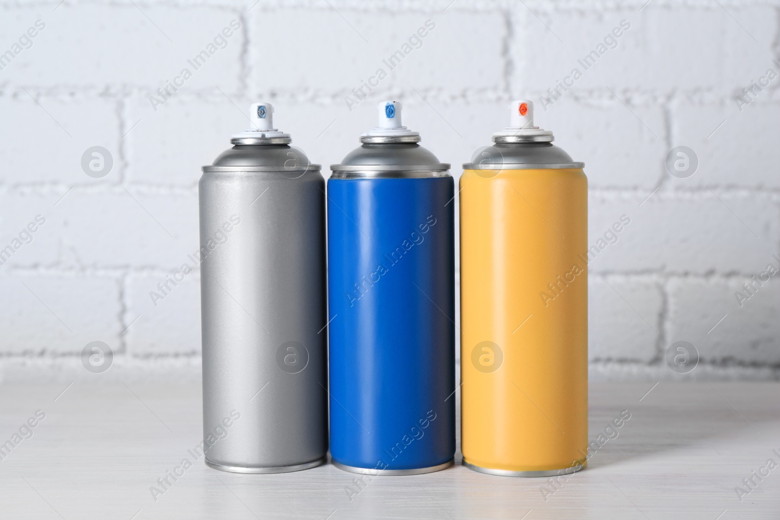 Photo of Cans of spray paint on wooden table near white brick wall