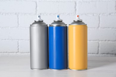 Photo of Cans of spray paint on wooden table near white brick wall