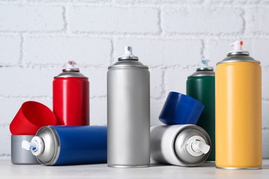 Photo of Cans of spray paint on wooden table near white brick wall